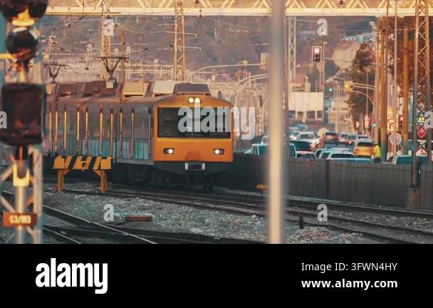 3 Line Rail Orange electric train moving along the railway line with city traffic ...
