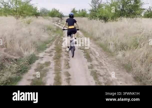 Woman Cycling on Dirt Trail Through Rural Field on Overcast Summer Day ...