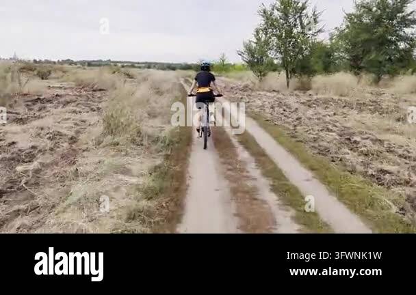 Woman Cycling on Dirt Trail Through Rural Field on Overcast Summer Day ...