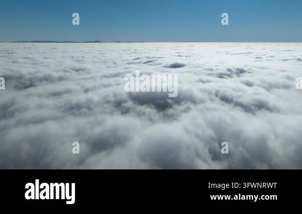 Aerial view flying over a vast sea of clouds under a clear blue sky ...