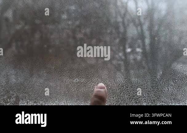 Condensation on window glass creates blurred effect while snow falls ...