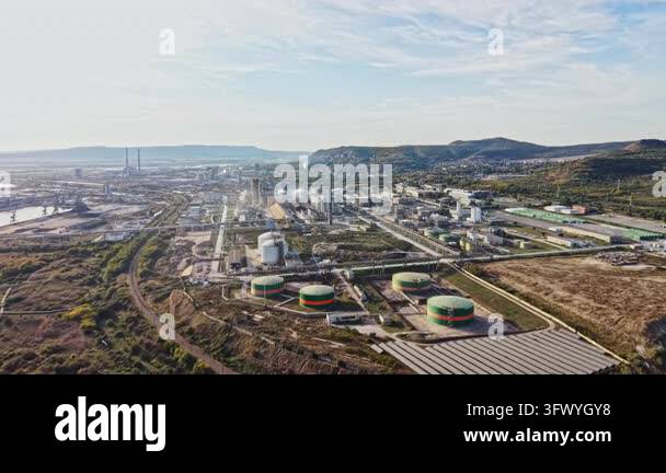 Refinery buildings, storage tanks, roads, and rail lines fill a valley ...