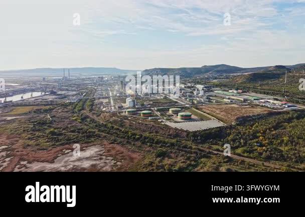 Refinery buildings, storage tanks, roads, and rail lines fill a valley ...