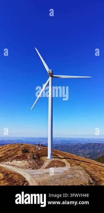 A wind turbine stands on a mountain ridge beside a winding dirt road ...