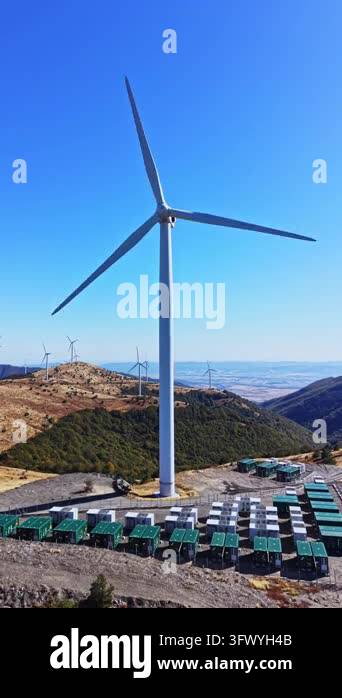 A wind turbine rises above rows of solar panels on a mountain ridge in ...