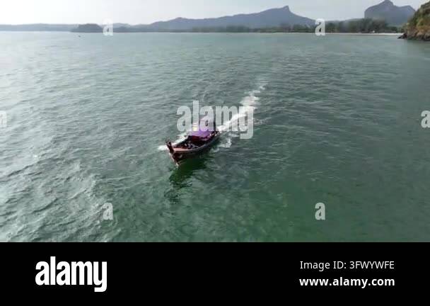 Aerial view of a longtail boat moving through the ocean near a tropical ...