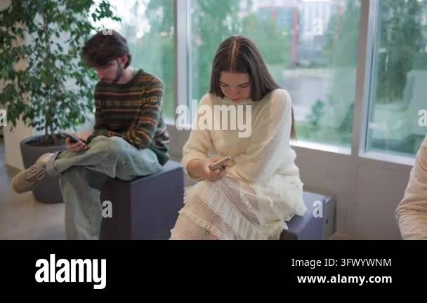 Three people sit in bright modern lounge in row, leaning forward with ...