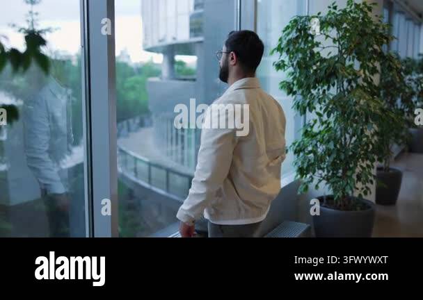 Calm, focused man with trimmed beard and glasses adjusts jacket sleeve ...