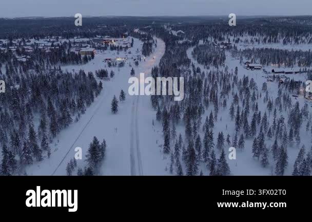 Flying forward over snowy taiga forest along a lit road toward an ...