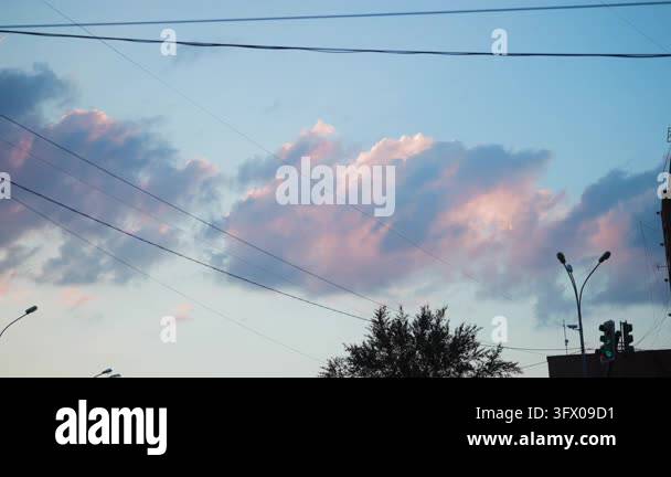 Cumulus clouds glow pink and blue over urban street at dusk, with ...