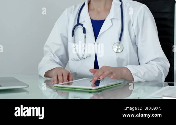 Medical doctor wearing a white lab coat and stethoscope, sitting at a ...