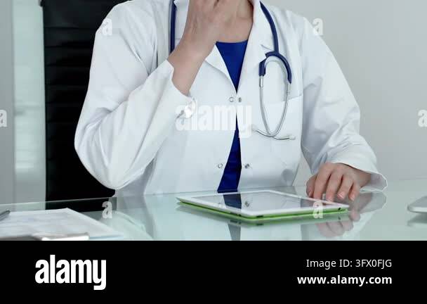 Medical doctor wearing a white lab coat and stethoscope, sitting at a ...