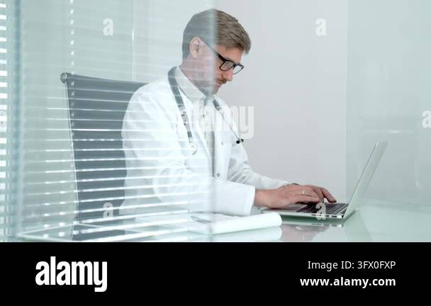 Male doctor wearing white coat and stethoscope using laptop computer ...