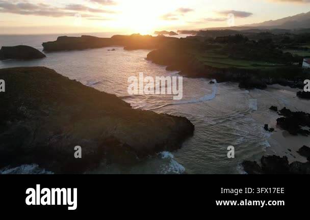 Aerial view of Barro Beach at sunrise with waves washing over a rocky ...