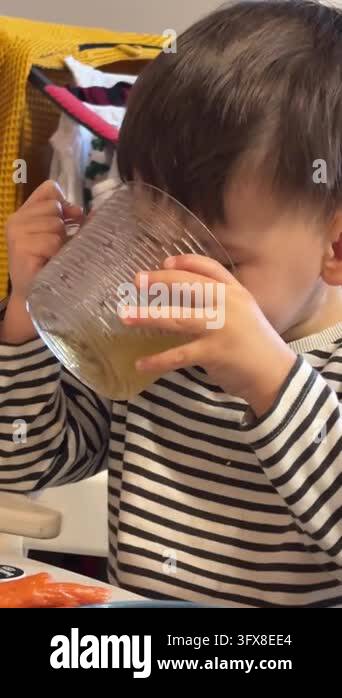 A toddler boy holds a large glass mug with both hands, drinks from it ...
