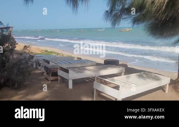 Rustic wooden sunbeds standing empty on a sandy beach with ocean waves ...