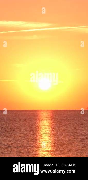 A sunset lights up the sky with orange and yellow hues over the ocean ...