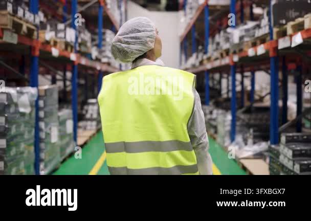 Large Warehouse Vector Rear view of a female worker in a safety vest walking through a large ...