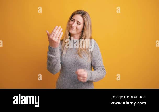 Playful blonde woman in a gray sweater making a beckoning hand gesture ...