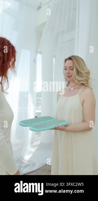 Two women handing a plate to each other, in brightly lit room with ...