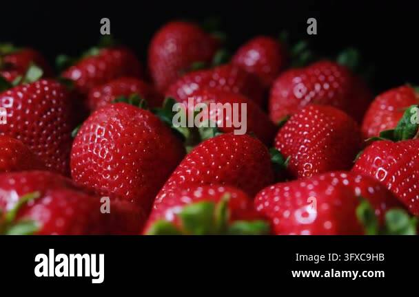 Macro view of fresh, ripe, red strawberries rotating slowly on a dark ...