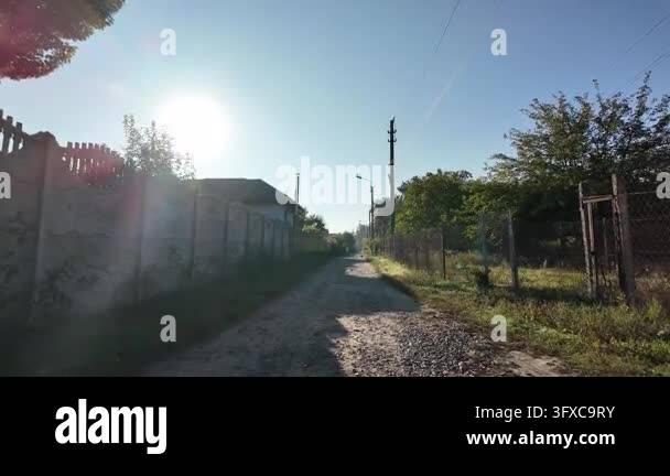 First-person POV walking along a narrow rural dirt road between garden ...