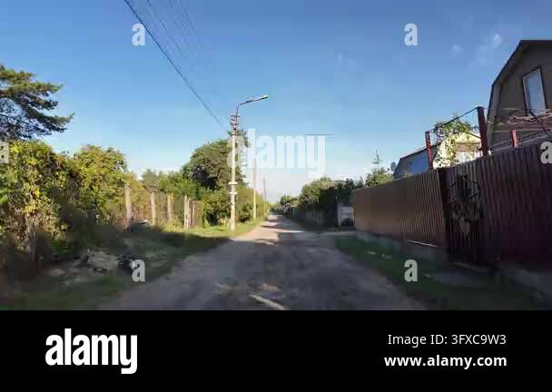 First-person POV walking along a narrow rural dirt road between garden ...