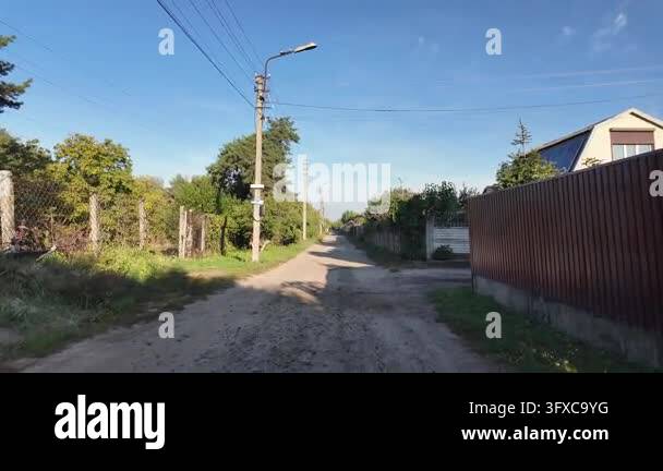 First-person POV walking along a narrow rural dirt road between garden ...