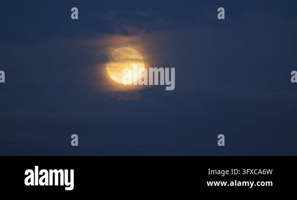 4k Moon Rising Full glowing moon rising through soft clouds in dark blue evening sky ...