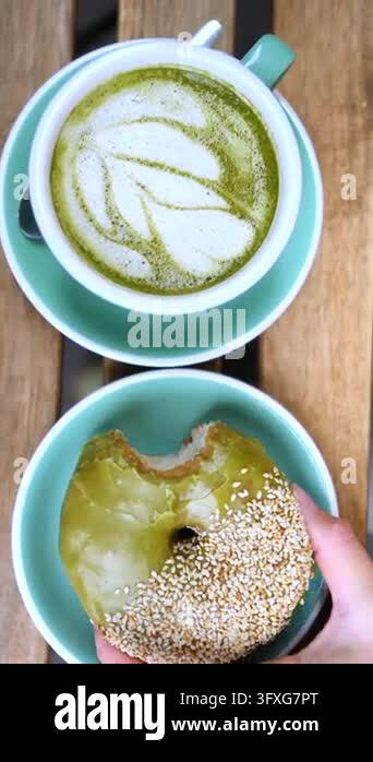 Turquoise cup of latte art sits above iced donut on wooden surface ...
