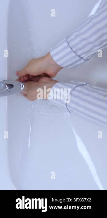Adult hands rinse in white sink, moving through soap and water with ...