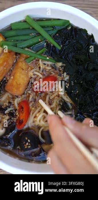 Rustic Asia Adult hand lifts noodles with chopsticks from steaming Asian noodle ...
