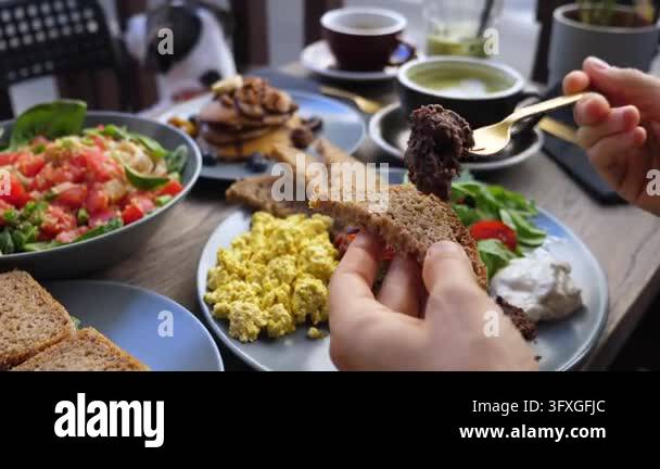 Toast Spoon Hands spread breakfast toast at shared brunch table. Gold fork and ...