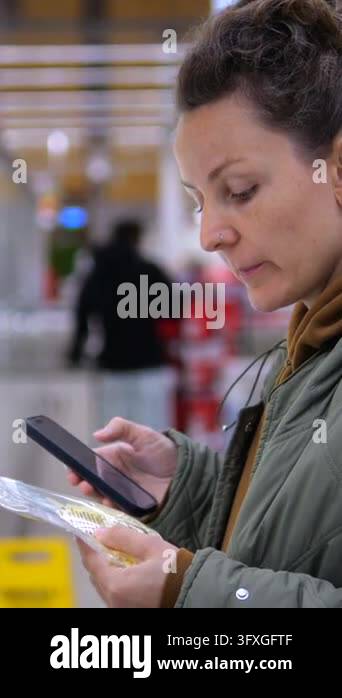 Woman checks food label with smartphone while shopping in grocery store ...