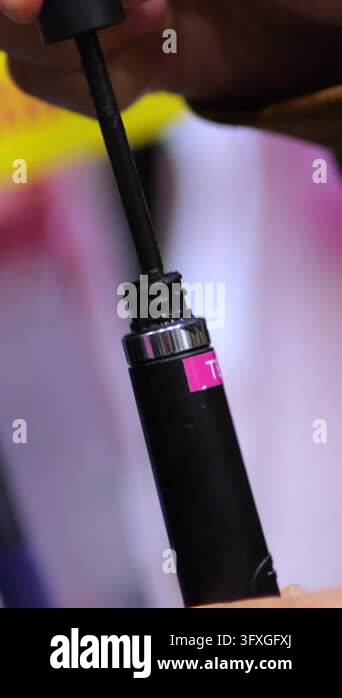 Black mascara tube is opened as hand draws out its wand and displays ...