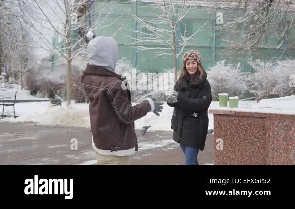 Cheerful young couple having fun playing with snow in a city park ...