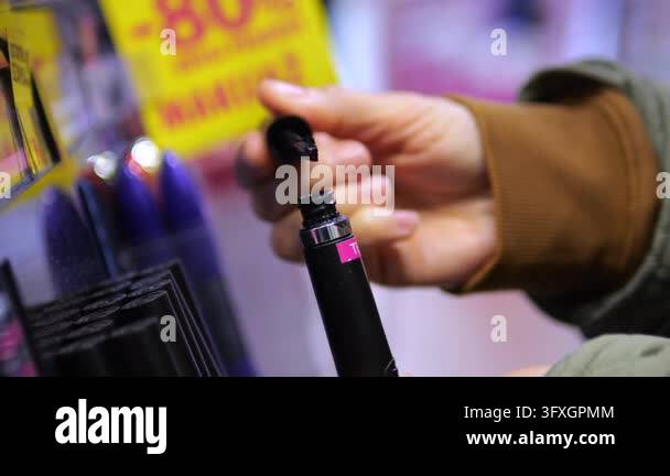 Hand tests black mascara wand at beauty counter, lifting applicator ...