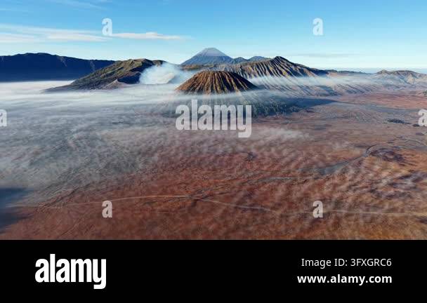 Valcano Red Mountains rise above misty, red earth. Vapor curls from active ...