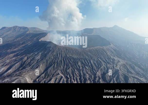 Volcano Smoking Volcano emits thick gray smoke into clear blue sky. Rugged, dark ...