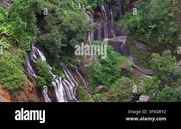 Towering waterfalls cascade over mossy rocks. Lush greenery surrounds ...