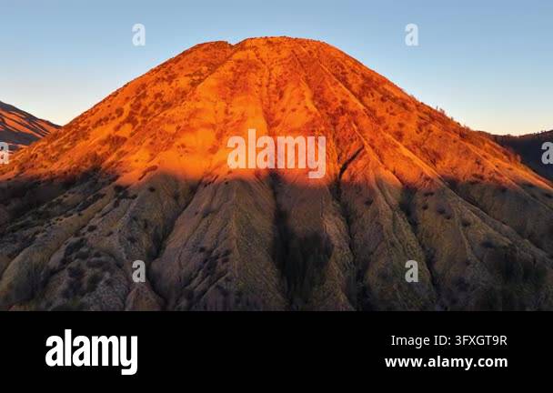 Sun glows warmly over rugged Mount Batok peak. Golden light paints ...