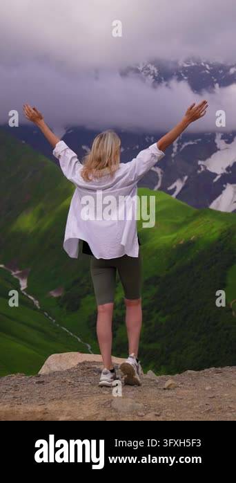 Snowing In Georgia Blonde woman standing on the edge of a cliff, raising her arms in a ...