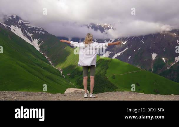 Snowing In Georgia Blissful woman standing on mountain peak with her hands raised ...