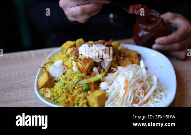 Hands spoon red sauce from jar onto plated vegetable rice and shredded ...