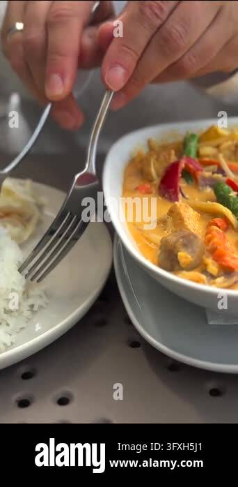 Fork and spoon guide rice into rich curry bowl while hands work over ...