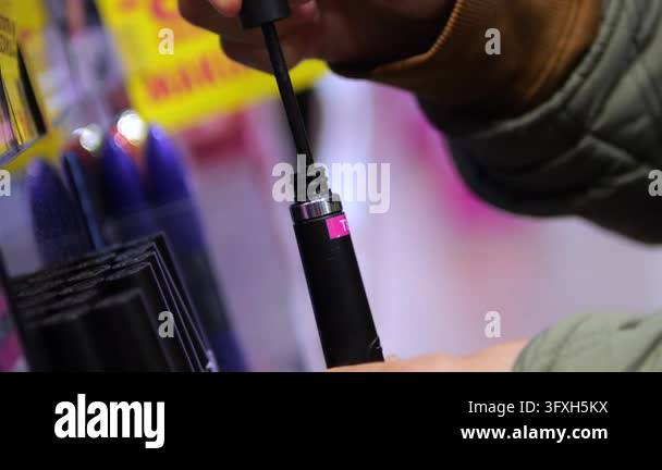Shopper removes mascara wand from black cosmetic tube at beauty counter ...