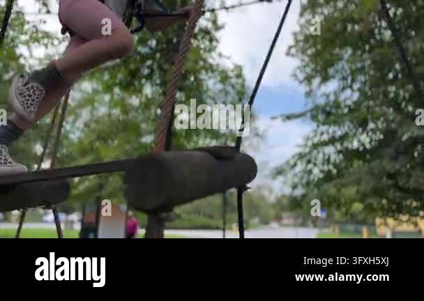 Young girl crosses suspended log ropes course, balancing between wooden ...