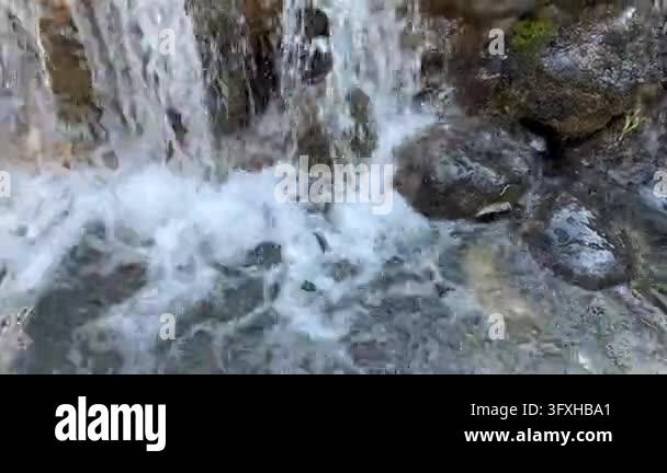 Close up of a small waterfall cascading over dark wet rocks with white ...