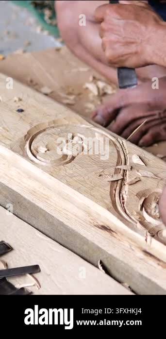 Wood carving artisan cuts ornamental pattern into soft wood with sharp ...