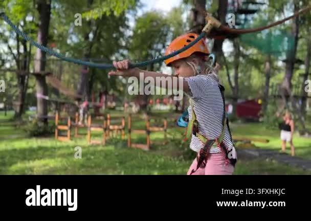 Young girl navigates ropes course while gripping overhead safety lines ...
